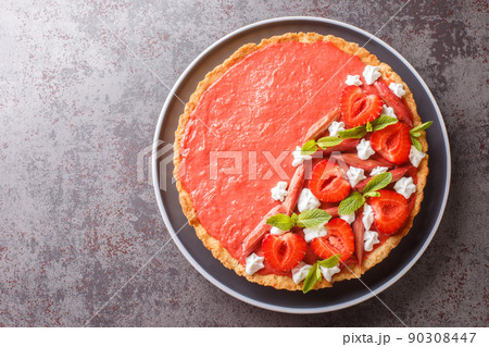 Festive tart with strawberry and rhubarb mousse, mint and whipped cream close-up on a plate. Horizontal top view 90308447