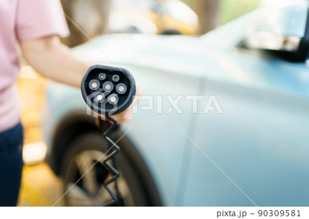Unrecognizable Asian woman holding AC type 2 EV charging connector at EV charging station, woman preparing an EV - electric vehicle charging connector for recharge a vehicle. 90309581