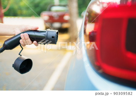 Unrecognizable Asian woman holding AC type 2 EV charging connector at EV charging station, woman preparing an EV - electric vehicle charging connector for recharge a vehicle. 90309582