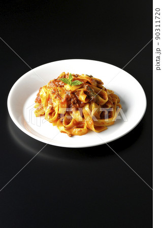 平打ちパスタのフィットチーネとトマトソースがよく絡んだボロネーゼを黒背景で撮影 90311720
