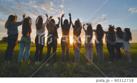 Silhouette of friends of 11 girls waving their hands at sunset in the field. 90312718