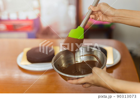 Woman mixing smooth delicious dark chocolate ganache with whisk in silver bowl. Woman mixing smooth delicious dark chocolate ganache with whisk in silver bowl. 90313073