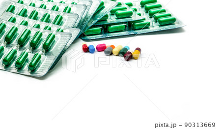 Green antibiotic capsule pill in blister pack and multicolored capsule pill on white background. Antibiotic drug resistance and prescription drugs concept. Pharmacy products. Pharmaceutical industry. 90313669