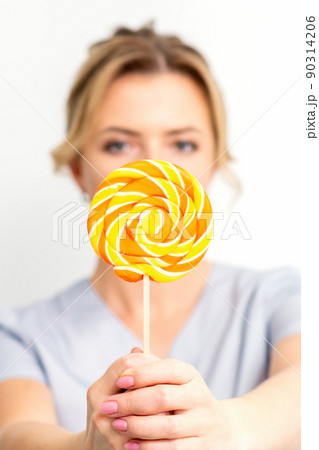Waxing, depilation concept. The beautician is wearing a medical coat holding a sugar lollipop on white background 90314206