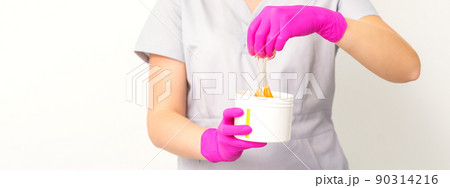 Portrait of a female caucasian beautician holding a jar of sugar paste for sugaring wearing pink gloves on white background Portrait of a female caucasian beautician holding a jar of sugar paste for sugaring wearing pink gloves on white background 90314216