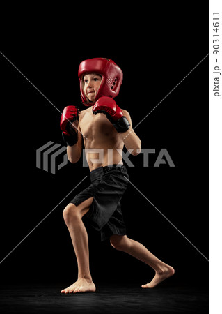 Studio shot of preschool boy, cute kid in sports shots and gloves training alone on black background. Sport, education, action, motion concept. 90314611