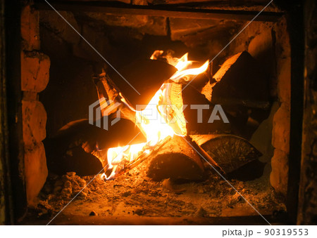 Warm light of a burning bright fire in a fireplace in old Russian stove. Flame and firewood background. Detail of interior. Warm light of a burning bright fire in a fireplace in old Russian stove. Flame and firewood background. Detail of interior. 90319553