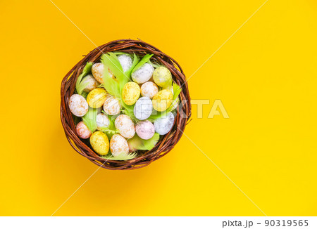 Easter composition with traditional decor. Small colorful eggs and feathers in wicker basket on soft background 90319565