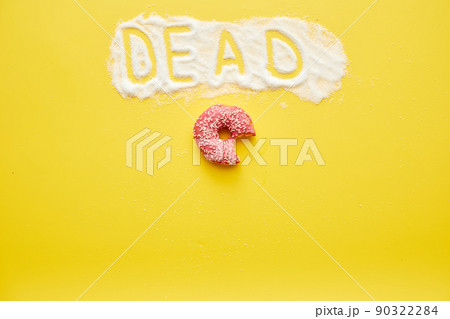 Half-eaten tasty doughnut with topping and dead word written on sugar powder, yellow background Half-eaten tasty doughnut with topping and dead word written on sugar powder, yellow background 90322284