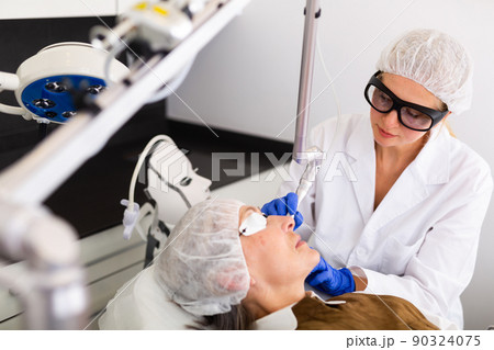 Cosmetologist making laser mole removal procedure for senior woman Cosmetologist making laser mole removal procedure for senior woman 90324075