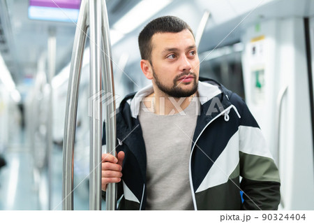 Young bearded man holding on handrails in subway car Young bearded man holding on handrails in subway car 90324404