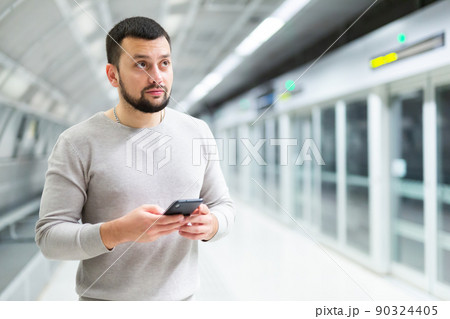 Guy traveler standing on subway station with phone in hands 90324405