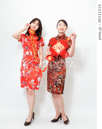 Asian women both wearing traditional cheongsam qipao dress hold Chinese festival couplet to celebrate new year with word meaning "May there be surplus year after year" on white background. 90331019