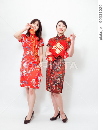 Asian women both wearing traditional cheongsam qipao dress hold Chinese festival couplet to celebrate new year with word meaning "May there be surplus year after year" on white background. Asian women both wearing traditional cheongsam qipao dress hold Chinese festival couplet to celebrate new year with word meaning "May there be surplus year after year" on white background. 90331020