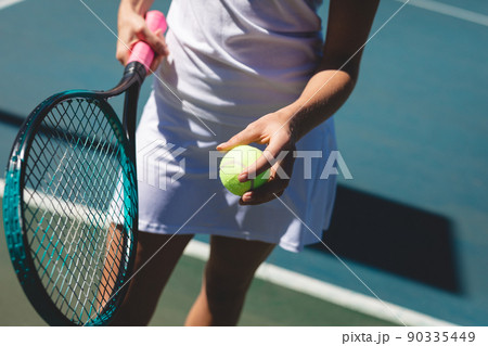 Midsection of young caucasian female tennis player standing with racket and ball at court 90335449