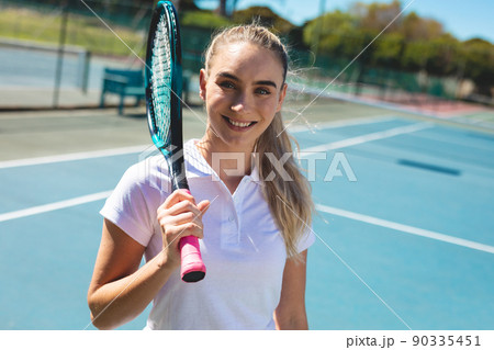 Portrait of smiling beautiful young caucasian female tennis player standing with racket at court 90335451