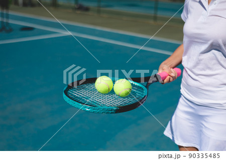 Midsection of young female caucasian athlete holding balls on tennis racket at court on sunny day Midsection of young female caucasian athlete holding balls on tennis racket at court on sunny day 90335485