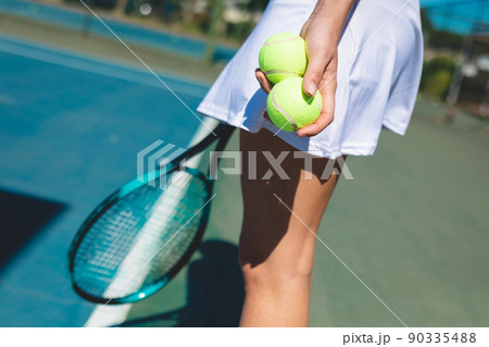 Side view midsection of young female caucasian athlete holding tennis balls at court on sunny day Side view midsection of young female caucasian athlete holding tennis balls at court on sunny day 90335488