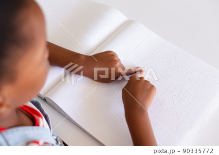 African american elementary schoolgirl touching braille book while studying at desk in class African american elementary schoolgirl touching braille book while studying at desk in class 90335772