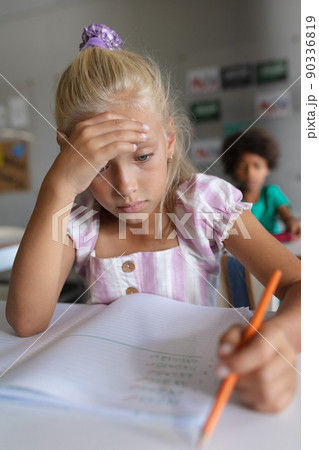Close-up of caucasian elementary schoolgirl with head in hand studying at desk in classroom Close-up of caucasian elementary schoolgirl with head in hand studying at desk in classroom 90336819