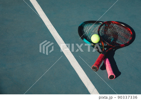 High angle view of rackets with ball by line on blue court during sunny day High angle view of rackets with ball by line on blue court during sunny day 90337336