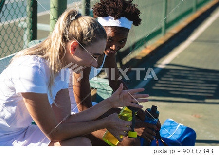 Happy multiracial female tennis players taking break while talking at court on sunny day 90337343