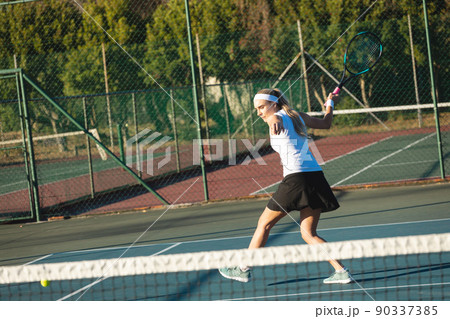 Full length of young female caucasian tennis player hitting ball at court on sunny day 90337385