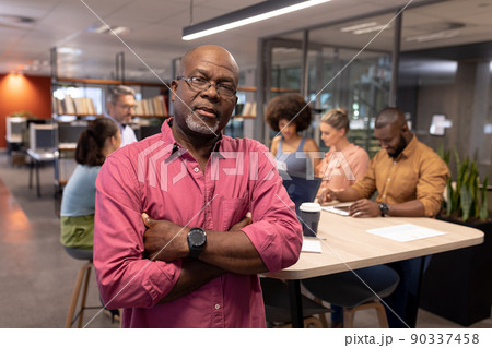 Portrait of confident mature african american businessman with arms crossed against colleagues Portrait of confident mature african american businessman with arms crossed against colleagues 90337458