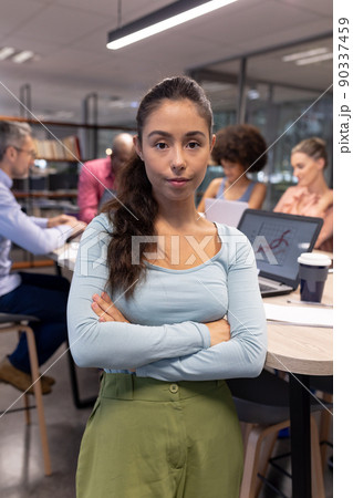 Portrait of confident hispanic young businessman with arms crossed against biracial colleagues 90337459