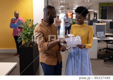 Happy african american businessman and businesswoman discussing over document at modern workplace 90337489