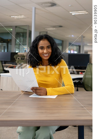 Portrait of smiling multiracial businesswoman with document sitting at desk in modern workplace Portrait of smiling multiracial businesswoman with document sitting at desk in modern workplace 90339905
