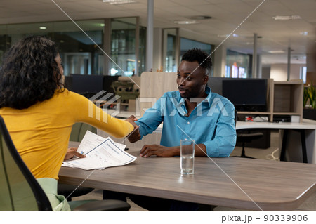 African american businessman doing hands shake with biracial businesswoman sitting at desk 90339906