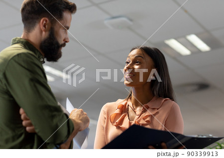 Happy biracial businesswoman discussing over document with caucasian businessman in workplace Happy biracial businesswoman discussing over document with caucasian businessman in workplace 90339913