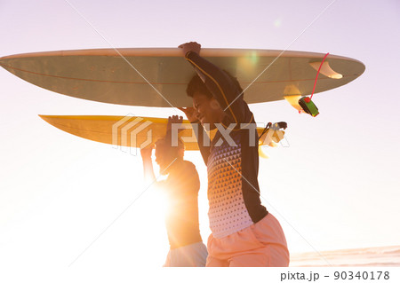 African american couple carrying surfboards on heads at beach against clear sky during sunset African american couple carrying surfboards on heads at beach against clear sky during sunset 90340178