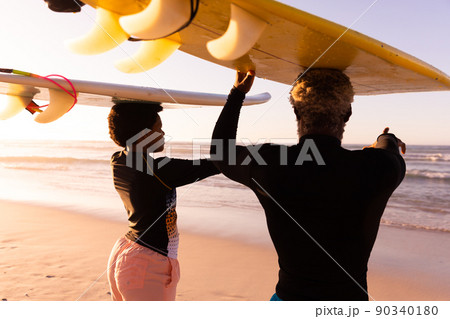 African american couple carrying surfboards on heads looking at sea against clear sky at sunset African american couple carrying surfboards on heads looking at sea against clear sky at sunset 90340180