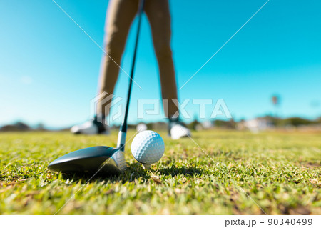 Low section of african american young man aiming ball with club at golf course against clear sky Low section of african american young man aiming ball with club at golf course against clear sky 90340499