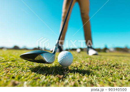 Low section of african american young man aiming ball with club at golf course against clear sky Low section of african american young man aiming ball with club at golf course against clear sky 90340500