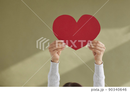 Woman holding up red mockup heart shaped valentine card against green background 90340646
