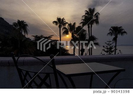 Sunset view through palm trees from balcony with table and chairs 90343398