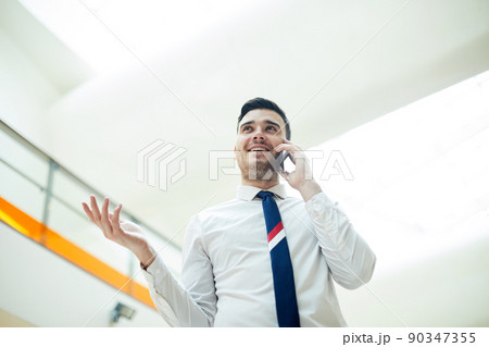 Content confident handsome business manager in white shirt talking to potential customer on mobile phone and gesturing hand Content confident handsome business manager in white shirt talking to potential customer on mobile phone and gesturing hand 90347355