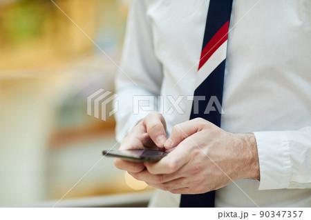 Close-up of unrecognizable bank employee in necktie and white shirt standing and making note in smartphone Close-up of unrecognizable bank employee in necktie and white shirt standing and making note in smartphone 90347357
