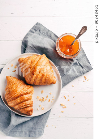 Plate with two fresh croissants and jam on white wooden table. Top view. 90348461