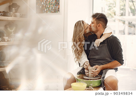 Mutual creative work. Young beautiful couple in casual clothes and aprons. People creating a bowl on a pottery wheel in a clay studio. 90349834