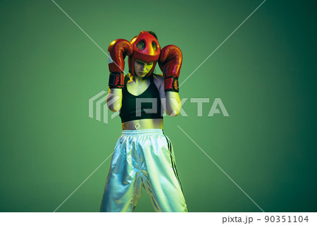 Cropped portrait of professional female boxer in sports protective equipment posing isolated on cyan color background in neon filter. Sport, competition, hobby, results, success concept Cropped portrait of professional female boxer in sports protective equipment posing isolated on cyan color background in neon filter. Sport, competition, hobby, results, success concept 90351104