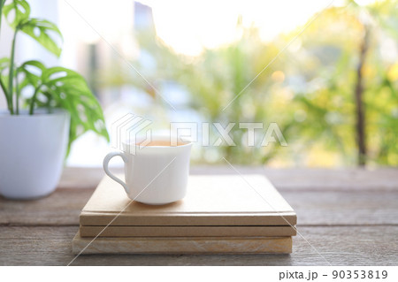Tea cup and brown kraft notebooks and Window Monstera obliqua leaf plant 90353819