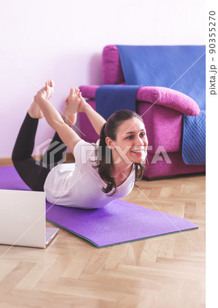 Young happy caucasian woman stretching in the living room while looking at her laptop. Health care and wellness at home concept. 90355270
