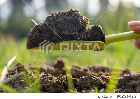 Close-up. A woman's hand loosens the ground in the garden with a garden shovel. Bright green grass and sun rays. Spring, earth care Close-up. A woman's hand loosens the ground in the garden with a garden shovel. Bright green grass and sun rays. Spring, earth care 90356435