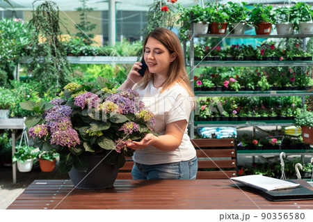 Portrait of garden center manager working with flowers and talking on phone 90356580