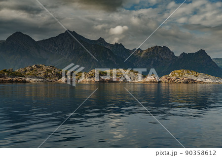 Norwegian seascape, rocky coast with dramatic skies, the sun breaks through the clouds, sheer cliffs, small islands illuminated by the sun 90358612