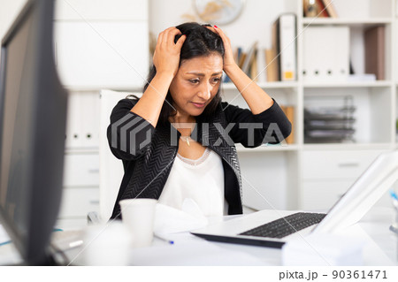 Troubled female manager looking at laptop in office 90361471